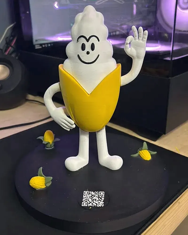 Figura de Mr. Grano sobre su base negra con elotes pequeños y código QR.